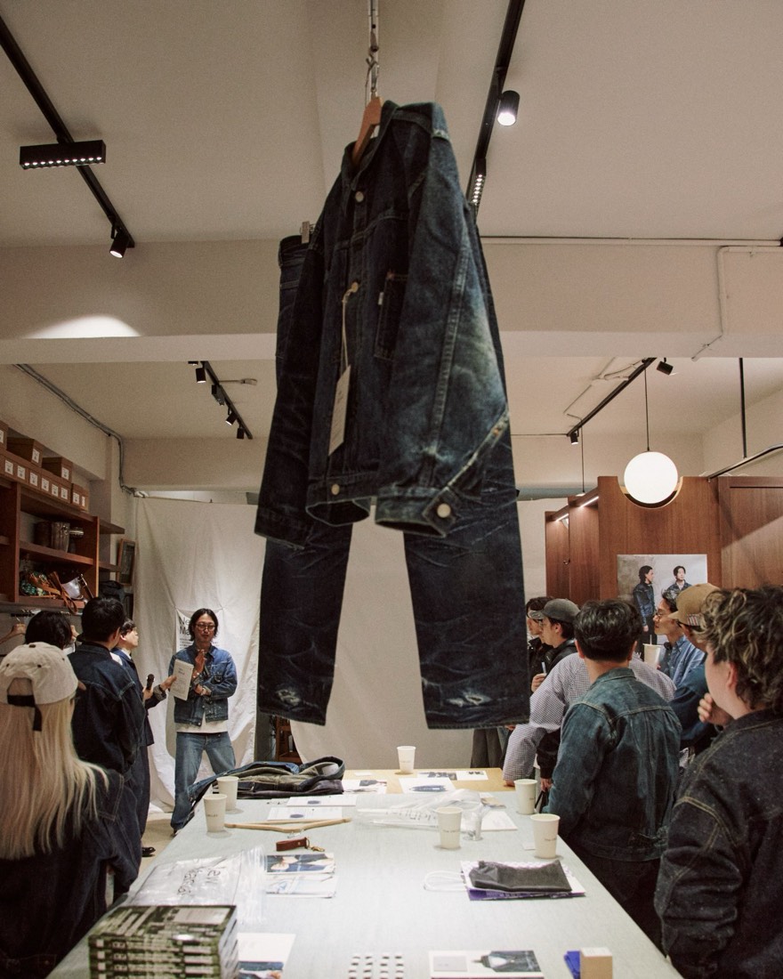 桌上展示丹寧外套，兩位背對鏡頭的人欣賞懸掛的外套