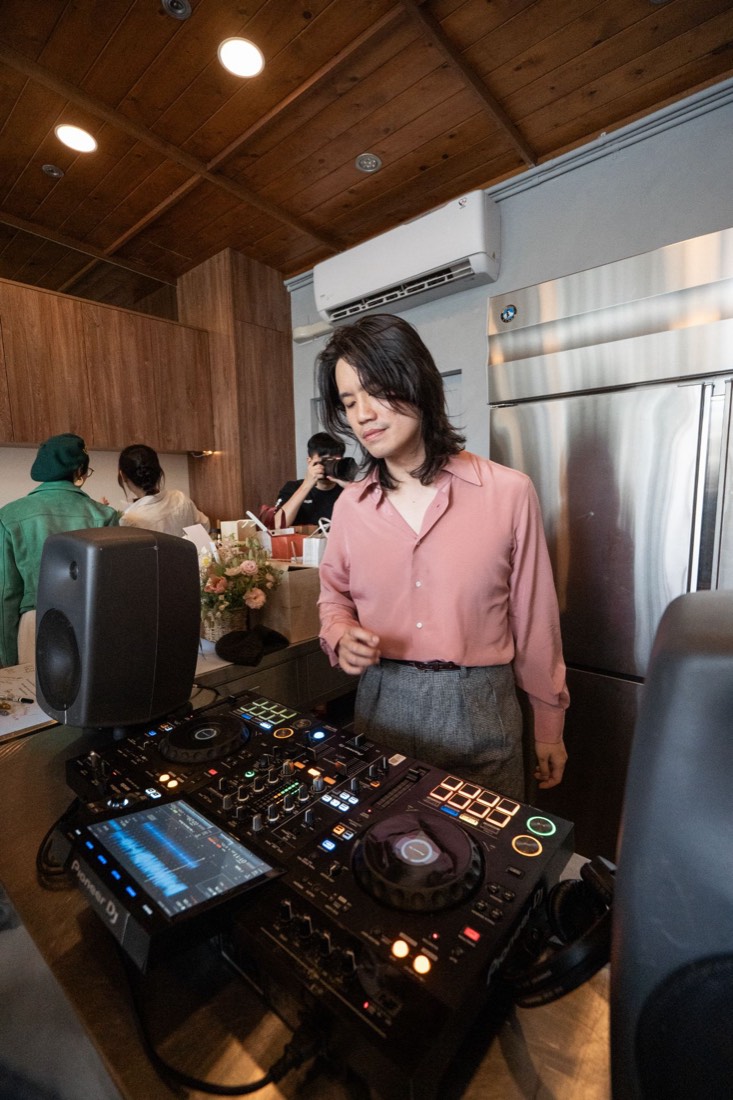 Gene 穿著粉色襯衫低頭在 DJ 台前