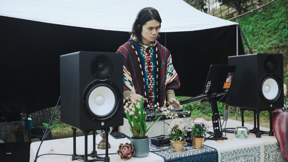 Gene 戴著耳機站在擺著花草的 DJ 桌後