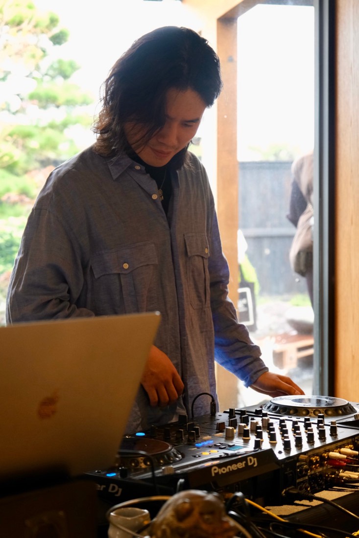 低頭操作 DJ 控台的特寫，背景是庭園的綠意