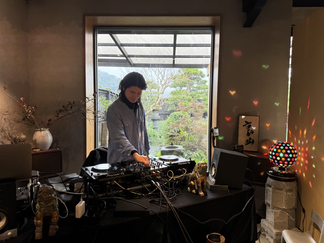 Gene 在窗前混音，牆上掛著「裏山」書法