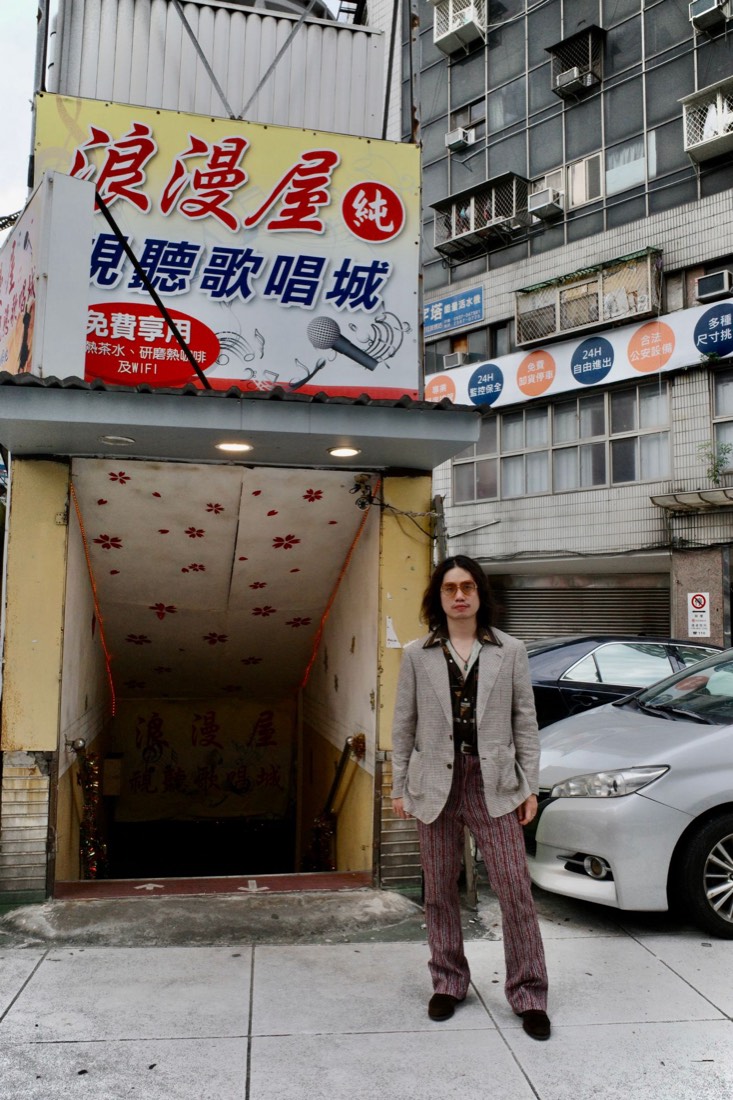 Gene 站在浪漫屋視聽歌唱城的入口樓梯前