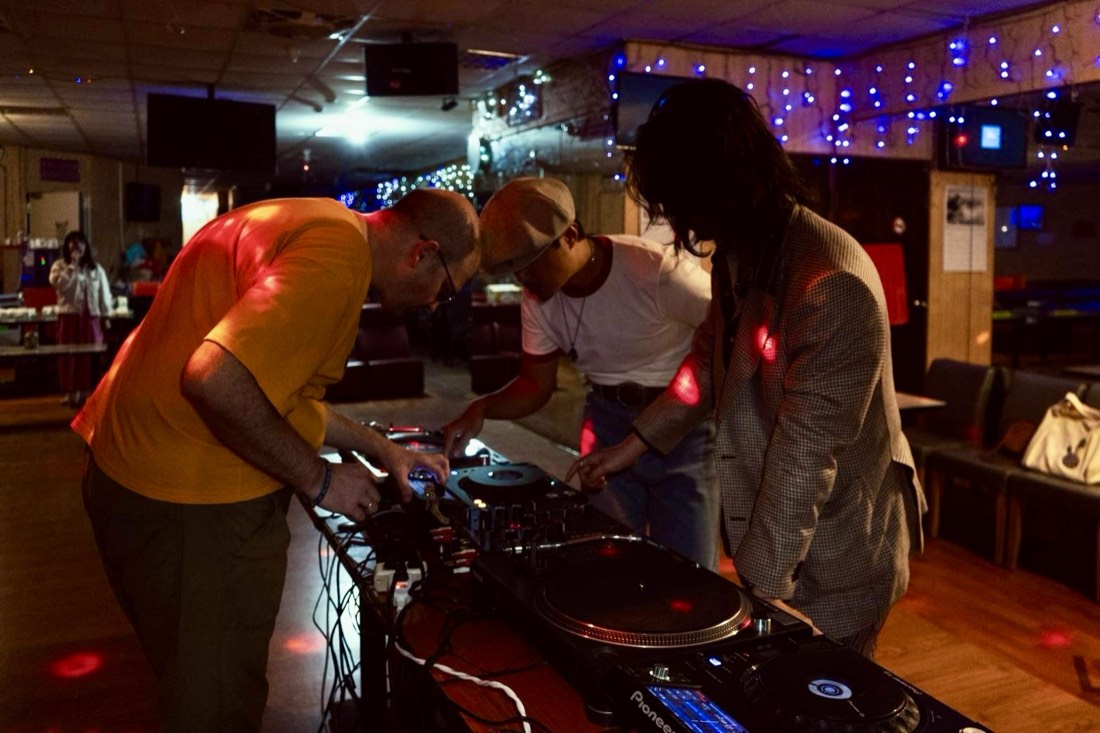 三位 DJ 低頭一起操作控台