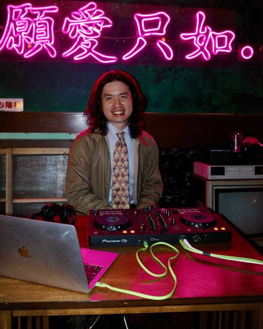 Gene 在霓虹燈招牌前坐在 DJ 台後微笑